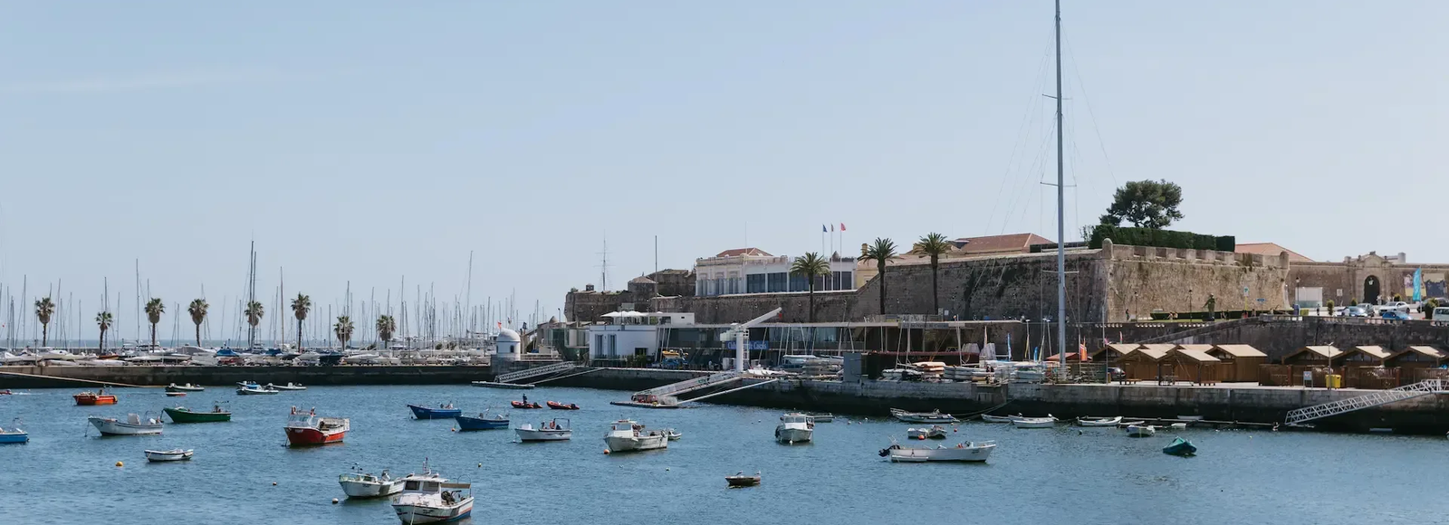 View of Cascais marina with small boats in the foreground and the historic Fortress of Nossa Senhora da Luz in the background.