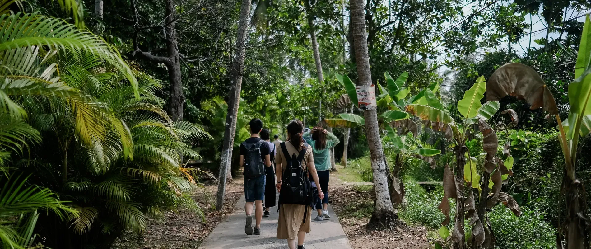 Small group walking along a tropical path surrounded by lush green trees and banana plants.