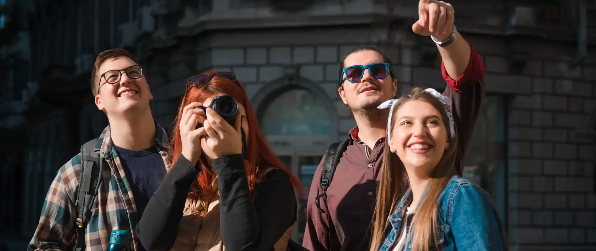 Young group of tourists enjoying a guided walking tour in a historic European city, smiling and taking photos as they explore urban landmarks.