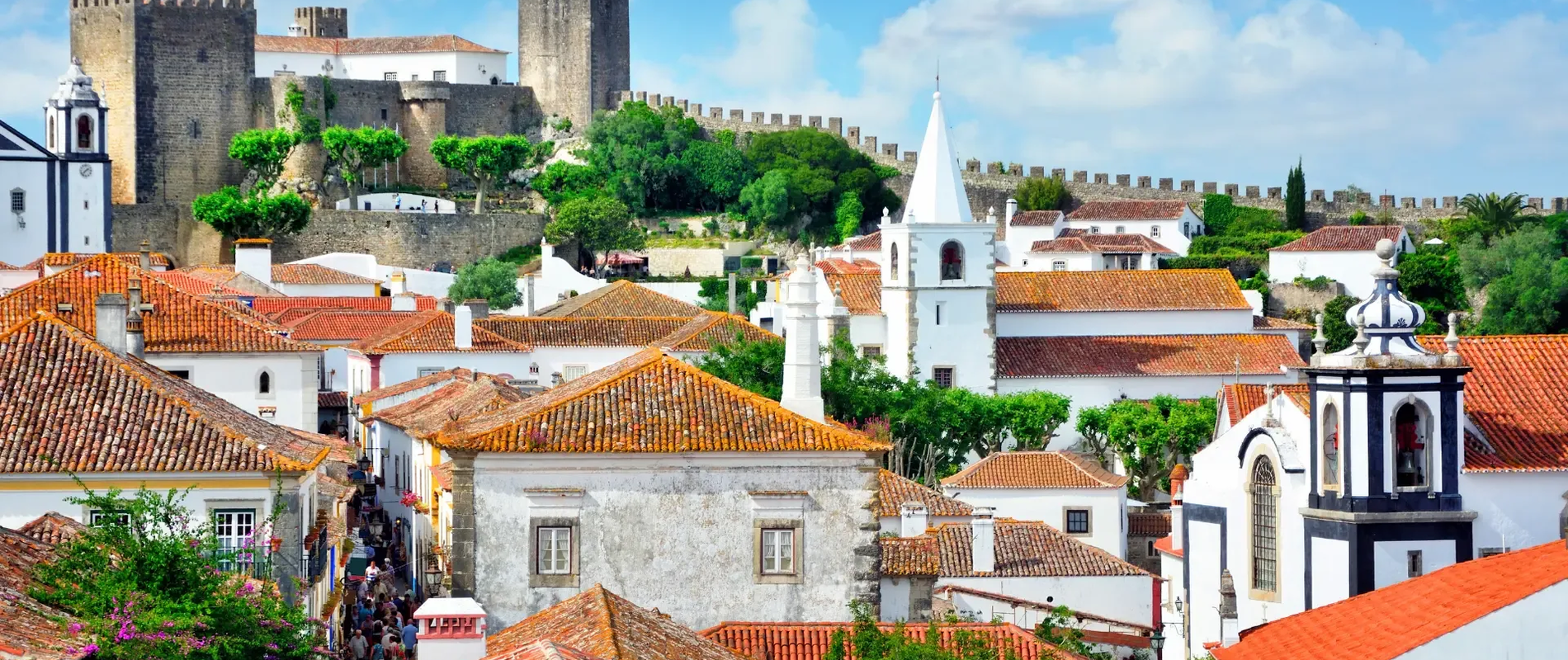 Panoramic view of the medieval town of Óbidos, Portugal, featuring whitewashed houses with red-tiled roofs and the castle surrounded by fortified walls.