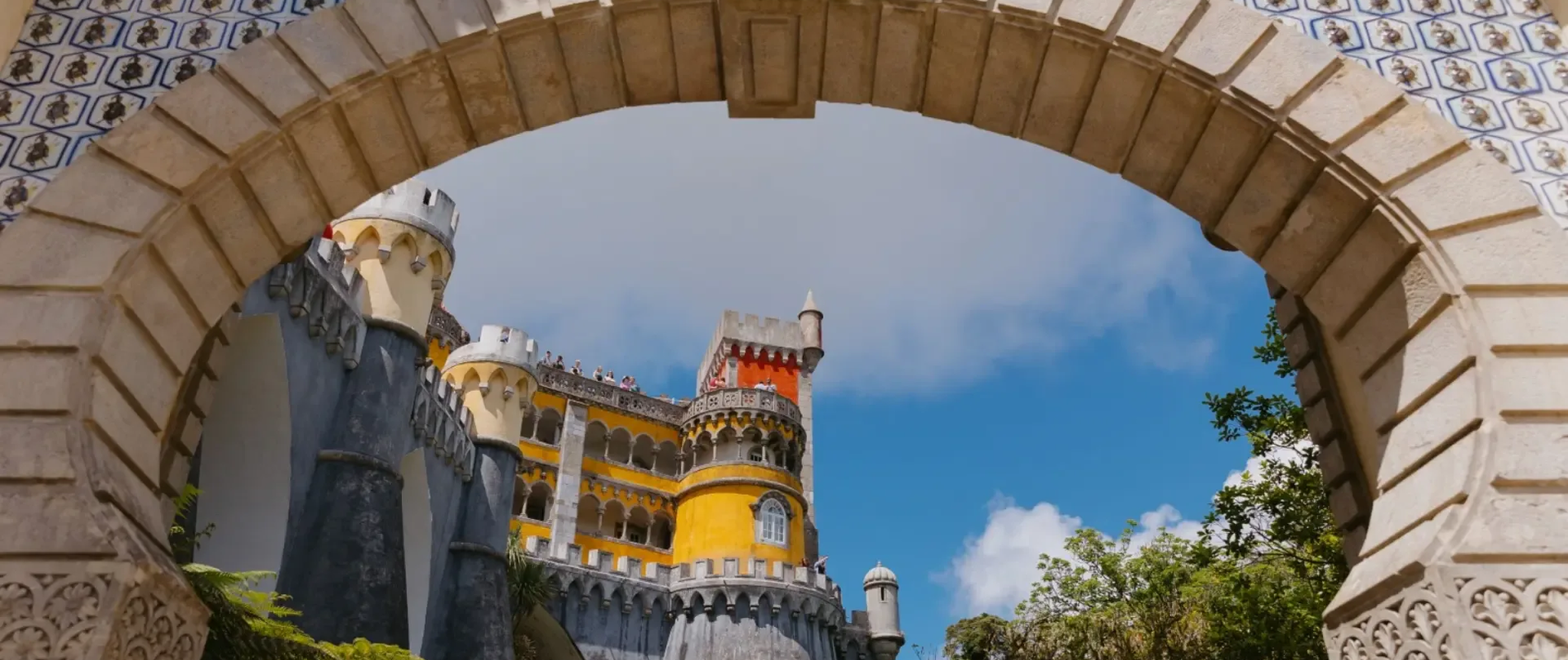 View of the colorful Pena Palace through the ornate tiled archway at the entrance, with blue sky in the background.