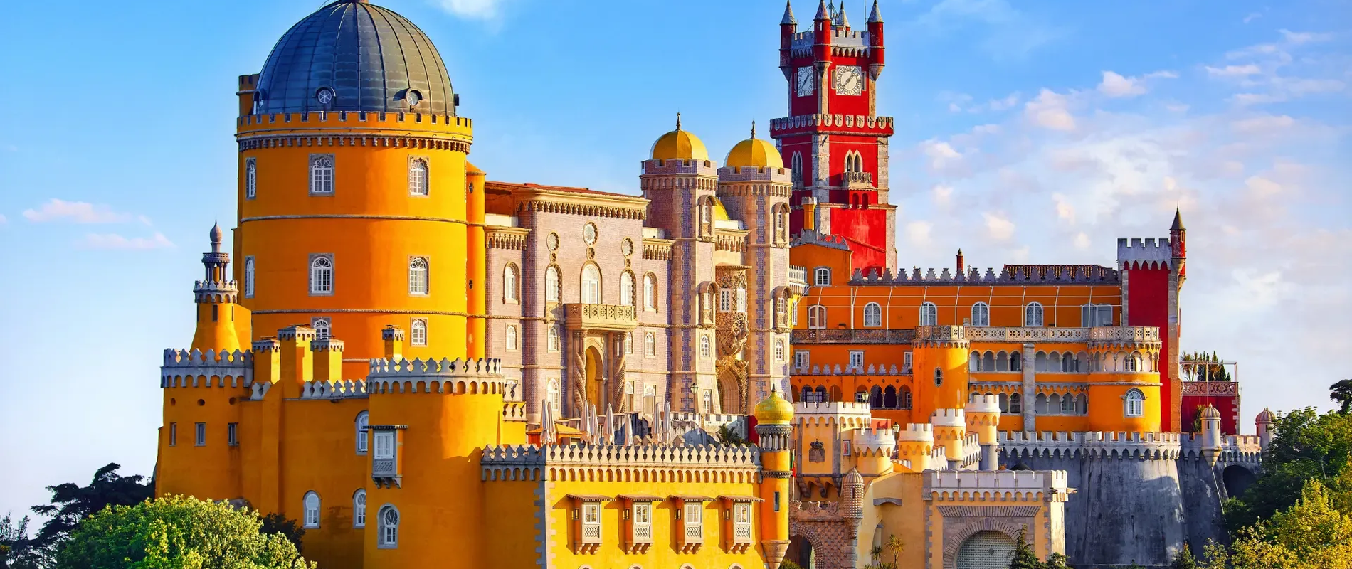 The colorful Pena Palace in Sintra, Portugal, showcasing romanticist architecture with vivid red, yellow, and grey towers under a clear blue sky.