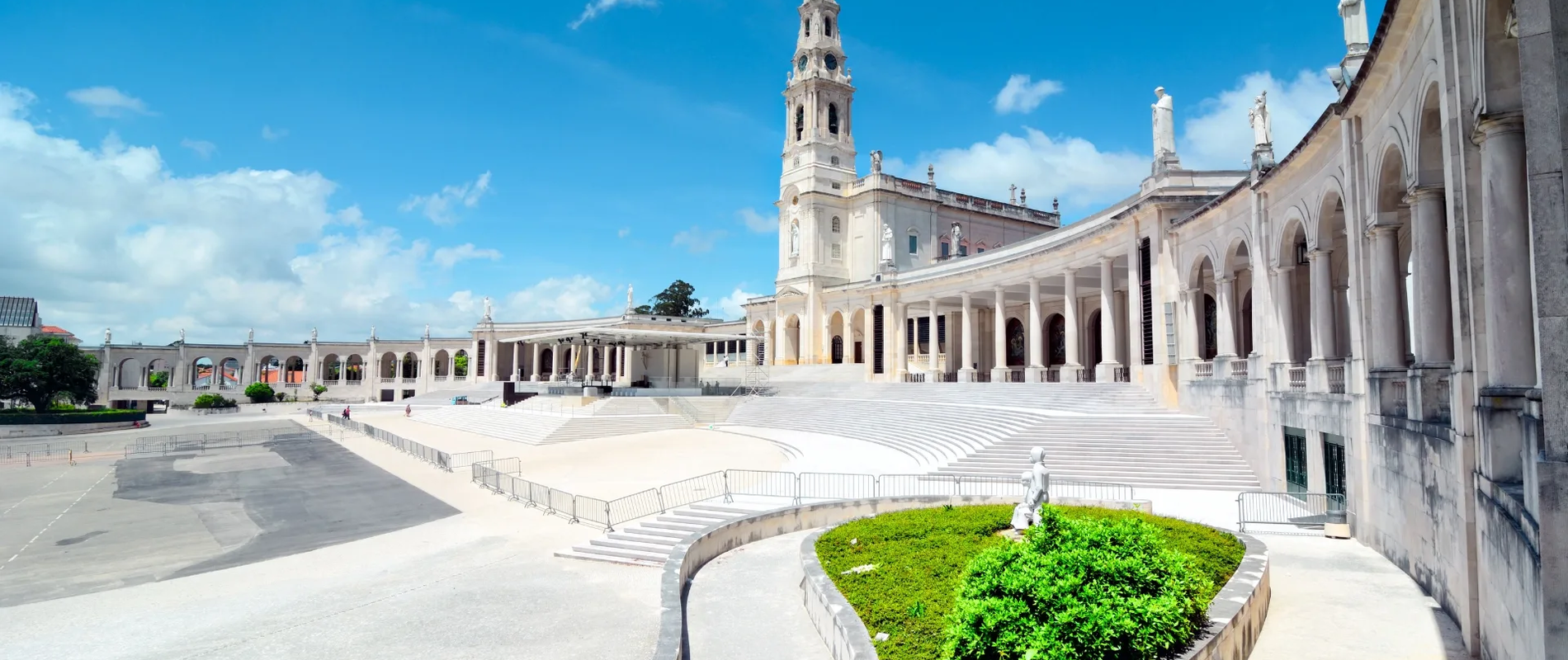 The Sanctuary of Fátima in Portugal, featuring the impressive neoclassical Basilica of Our Lady of the Rosary, colonnades, and statues under a clear blue sky.