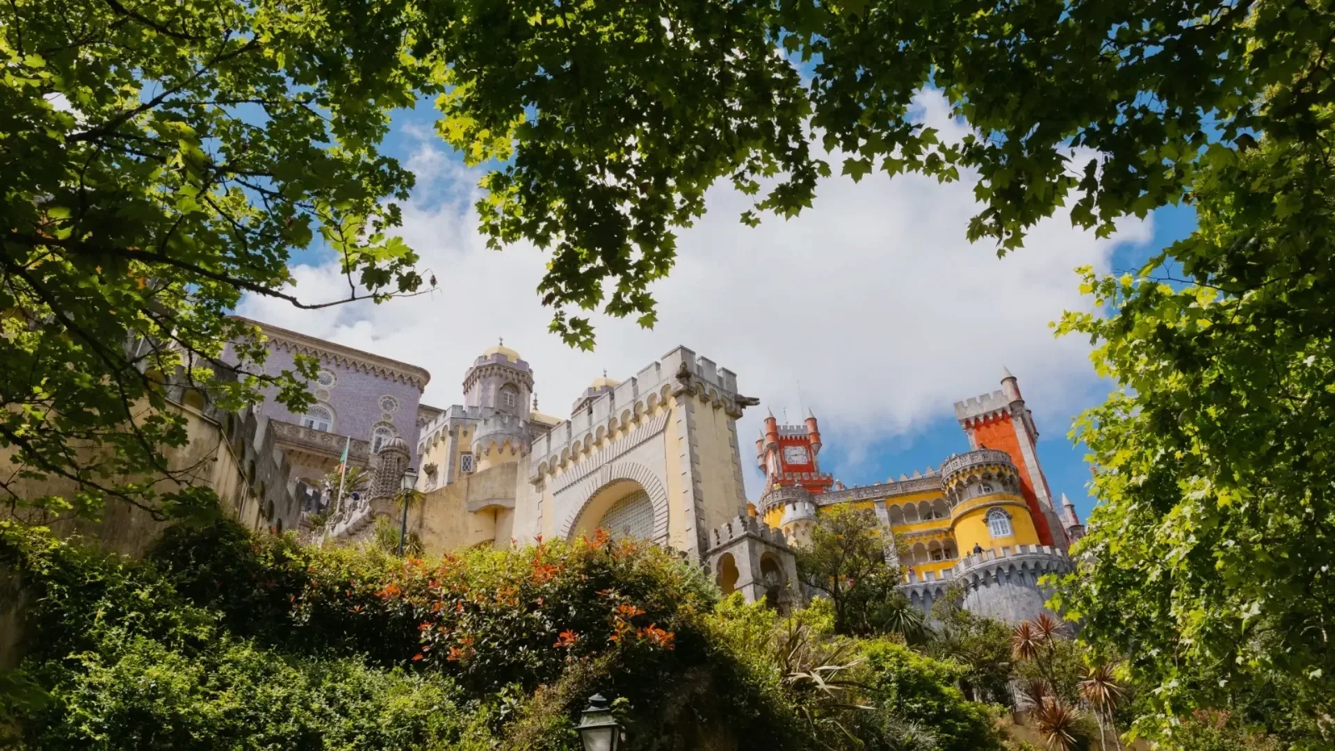 Pena Palace in Sintra, Portugal, viewed through green tree branches on a sunny day.