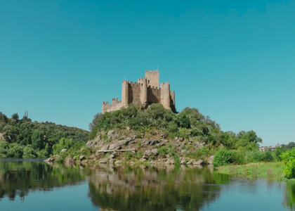 Panoramic view of Almourol Castle on an island in the Tagus River, Portugal, with clear blue skies and water reflection.