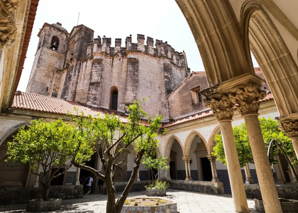 View of the Cloister of Santa Bárbara and the Charola tower at the Convent of Christ in Tomar, Portugal, showcasing Gothic and Manueline architecture.