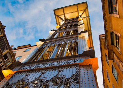 Santa Justa Lift in Lisbon, Portugal, seen from below with neo-Gothic ironwork and glowing lights at dusk.