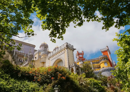 Pena Palace in Sintra, Portugal, viewed through green tree branches on a sunny day.