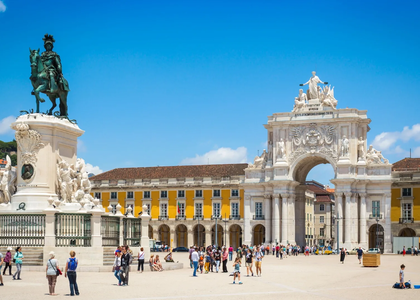 Commerce Square in Lisbon on a sunny day, featuring the equestrian statue of King José I and the iconic Rua Augusta Arch, with people walking around.