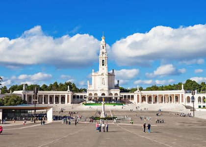 Sanctuary of Fátima in Portugal with the Basilica of Our Lady of the Rosary and pilgrims walking across the esplanade under a bright blue sky.