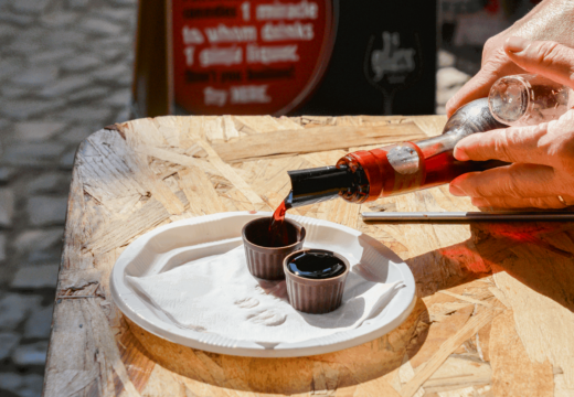 Hands pouring Ginja liqueur into small edible chocolate cups during a tasting session in the medieval village of Óbidos, Portugal. A traditional cherry liqueur experience served on a rustic wooden table.