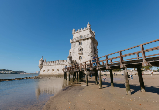 View of the Belém Tower by the Tagus River in Lisbon, with people walking on the wooden bridge on a sunny day