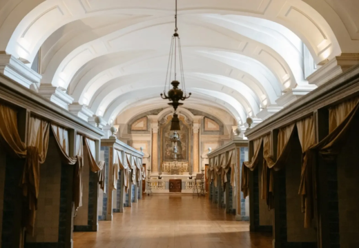 Historic infirmary of the Mafra National Palace, with vaulted ceilings, draped patient cubicles, and a baroque chapel altar at the far end.