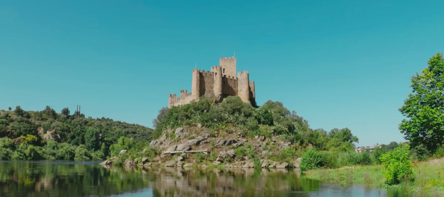 Panoramic view of Almourol Castle on an island in the Tagus River, Portugal, with clear blue skies and water reflection.