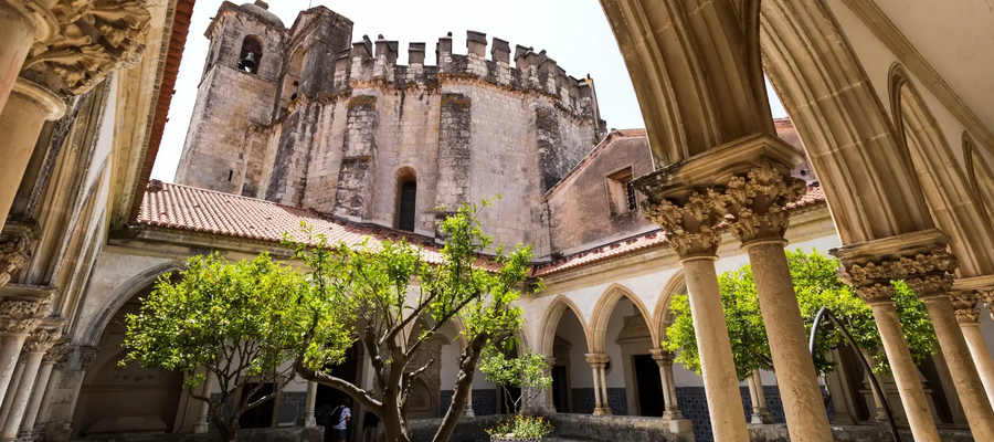 View of the Cloister of Santa Bárbara and the Charola tower at the Convent of Christ in Tomar, Portugal, showcasing Gothic and Manueline architecture.
