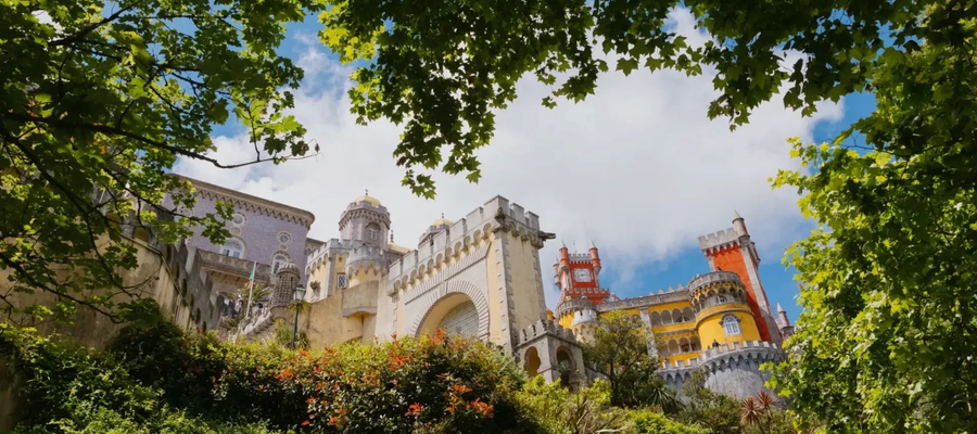 Pena Palace in Sintra, Portugal, viewed through green tree branches on a sunny day.