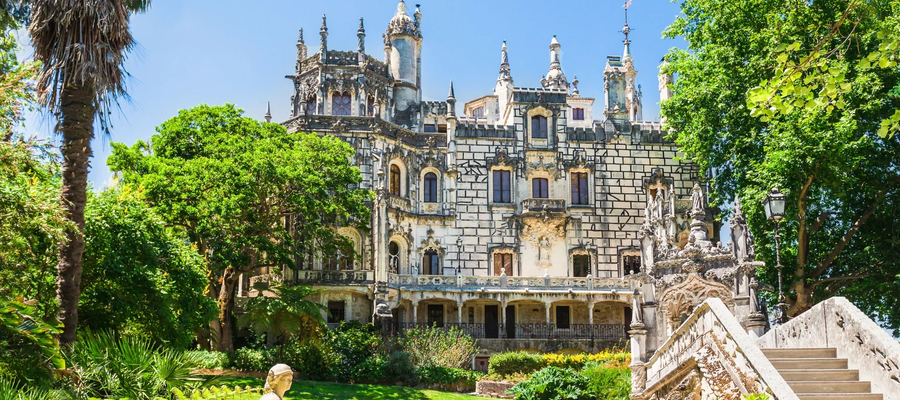 Palácio da Quinta da Regaleira em Sintra, rodeado por jardins exuberantes e arquitetura neomanuelina.