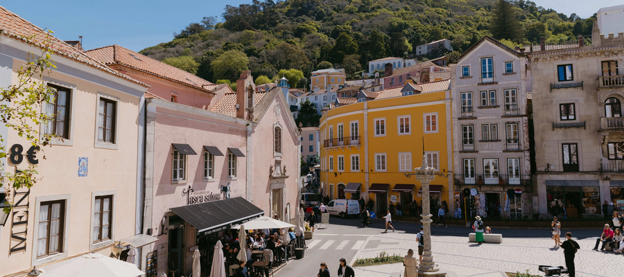 View of the historic center of Sintra, Portugal, with colorful buildings, outdoor cafes, and the Moorish Castle on the hilltop.