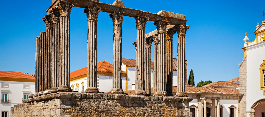 Roman Temple of Évora, Portugal, with tall Corinthian columns standing in the historic city center, under a clear blue sky.