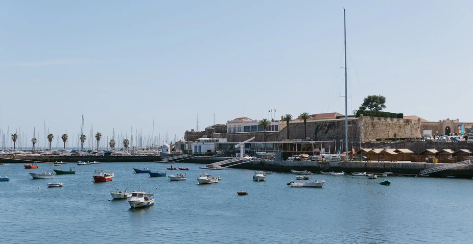 View of Cascais marina with small boats in the foreground and the historic Fortress of Nossa Senhora da Luz in the background.