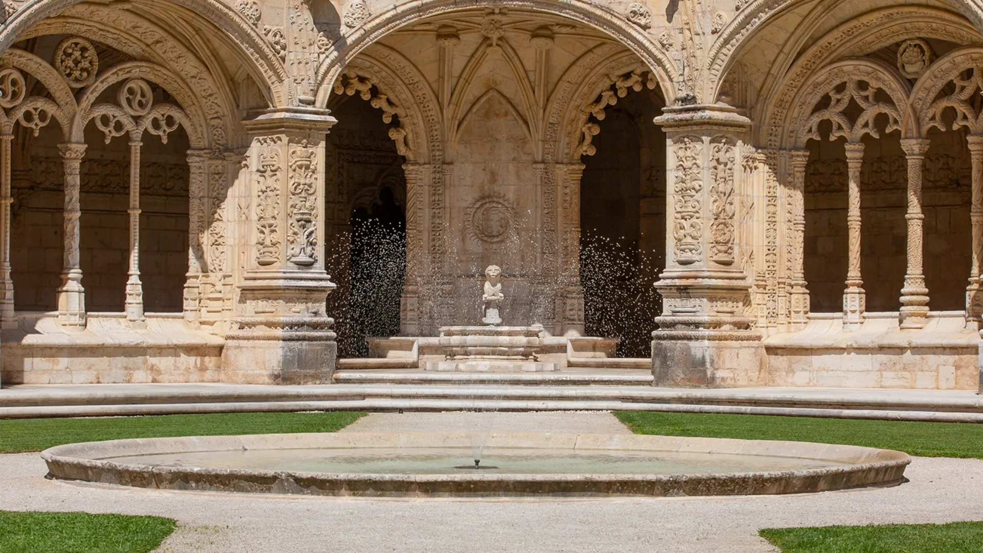 Manueline-style cloister of the Jerónimos Monastery in Lisbon, Portugal, with ornate arches and a central fountain.