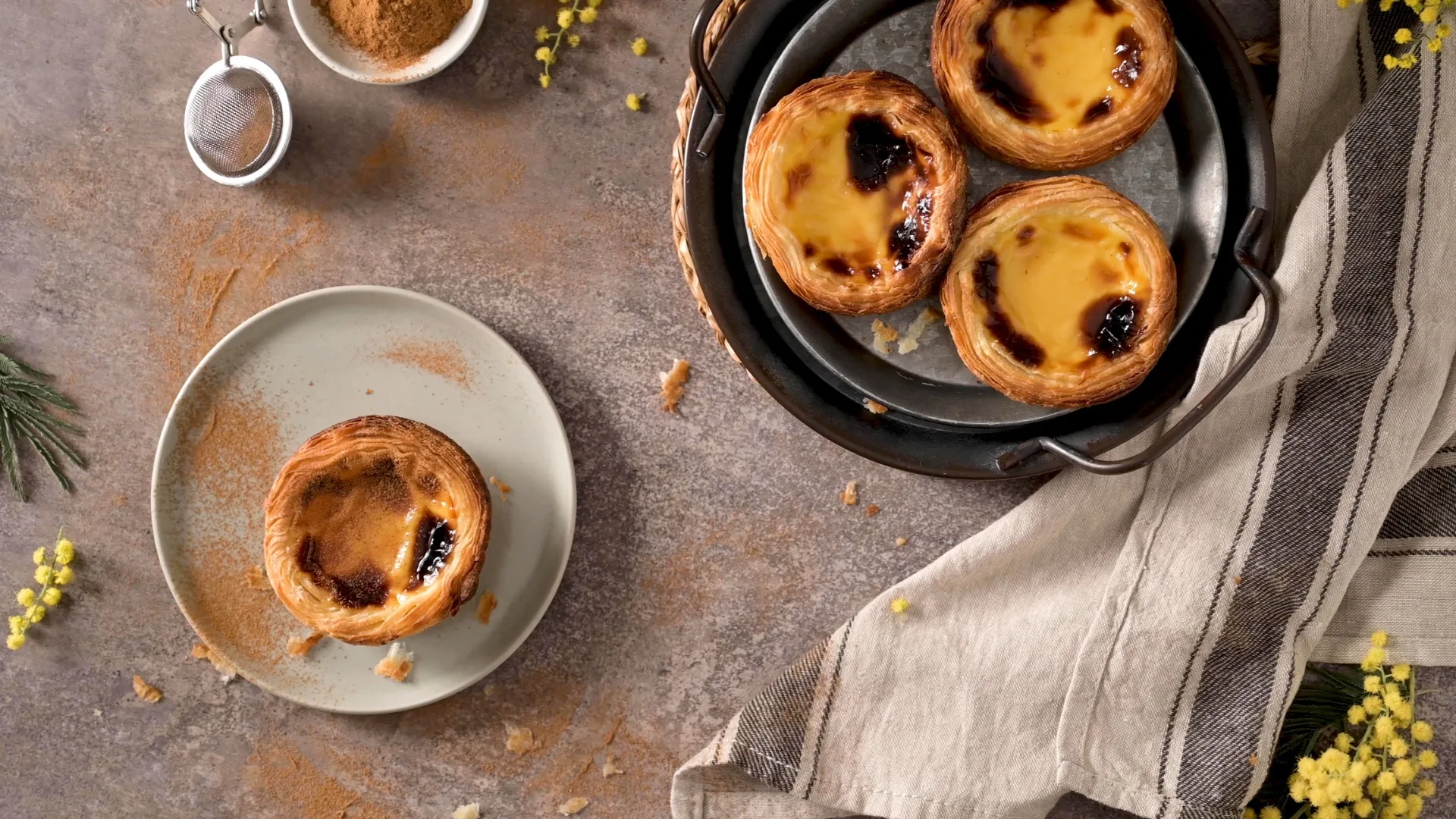 Top view of Portuguese custard tarts (Pastéis de Nata) served on a plate and tray, with cinnamon powder and a rustic setting.