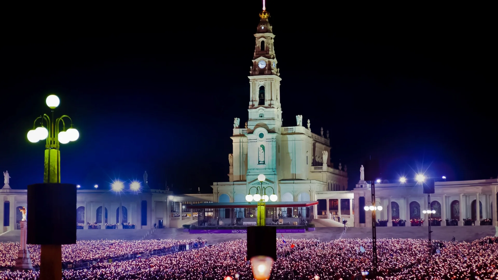 Night candlelight procession at the Sanctuary of Fátima in Portugal, with thousands of pilgrims holding candles in front of the illuminated Basilica of Our Lady of the Rosary.