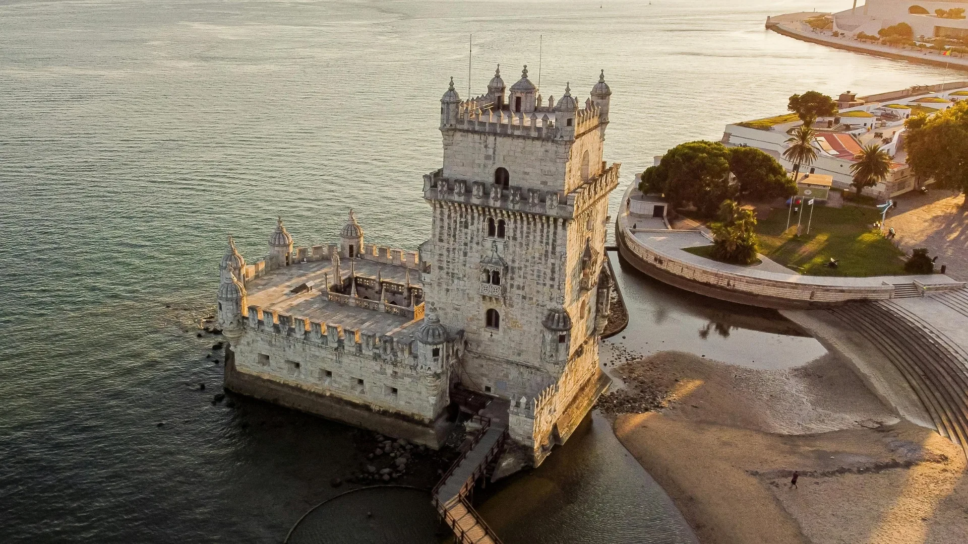 Aerial view of the historic Belém Tower in Lisbon, Portugal, at the edge of the Tagus River during sunset.