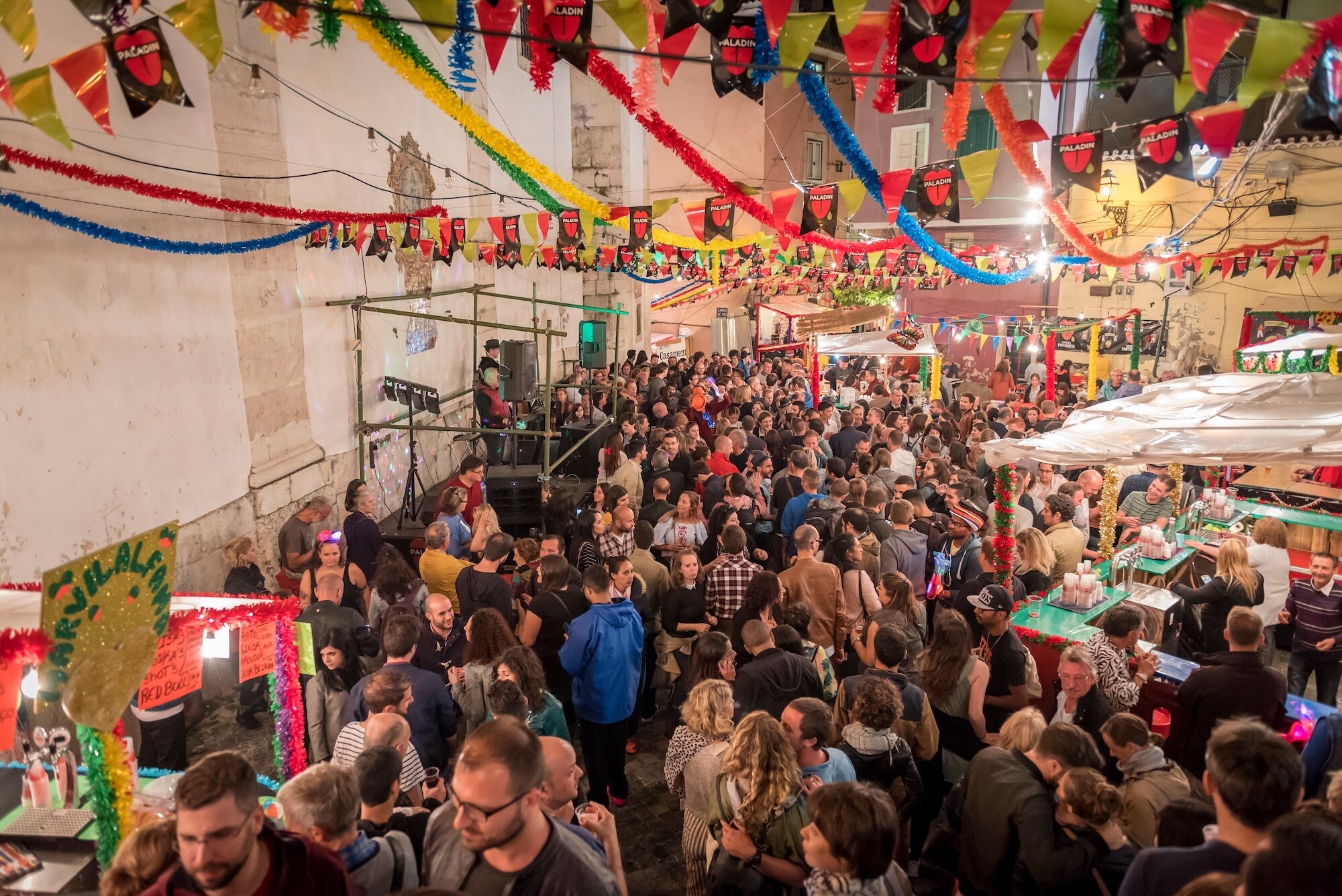 Crowd enjoying the Popular Saints Festival in Alfama, Lisbon, with food stalls, music, and colorful decorations