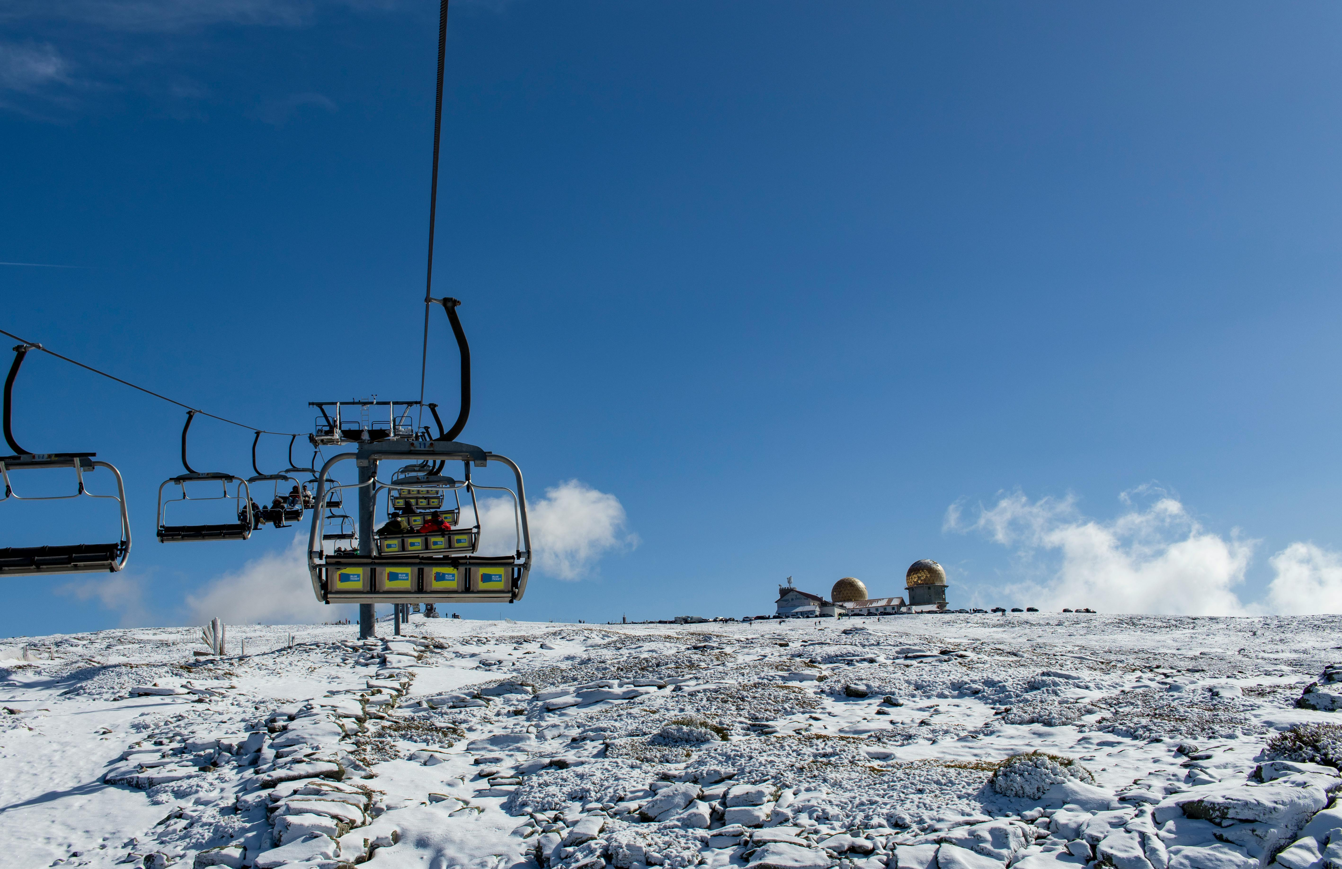 Ski lift ascending a snowy slope in Serra da Estrela, with radar domes in the distance under a blue sky
