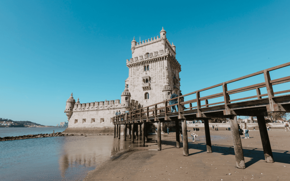View of Belém Tower in Lisbon, Portugal, with its detailed Manueline architecture, wooden bridge access, and calm waterfront at low tide. A historic maritime defense structure and iconic landmark on the Tagus River.