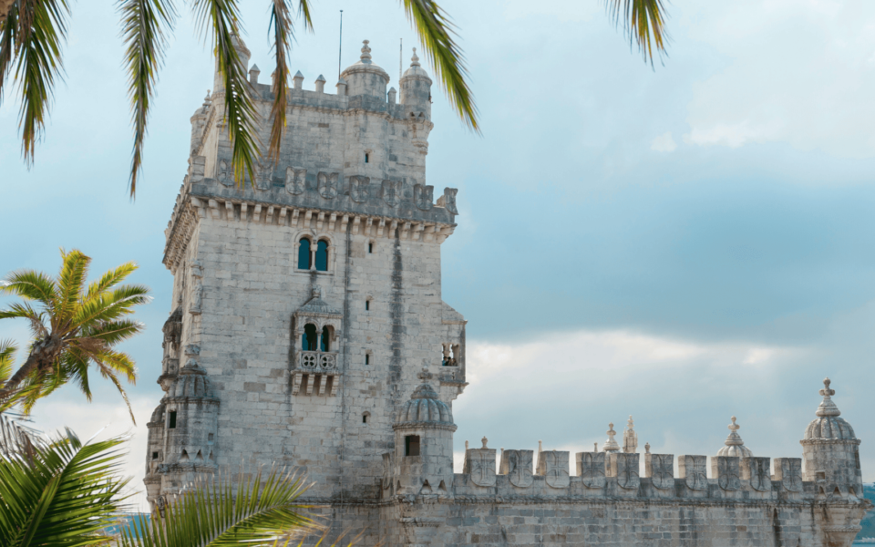 Scenic view of Belém Tower in Lisbon, Portugal, framed by palm trees under a cloudy sky. The Manueline-style monument stands out as one of the city’s most iconic architectural landmarks.