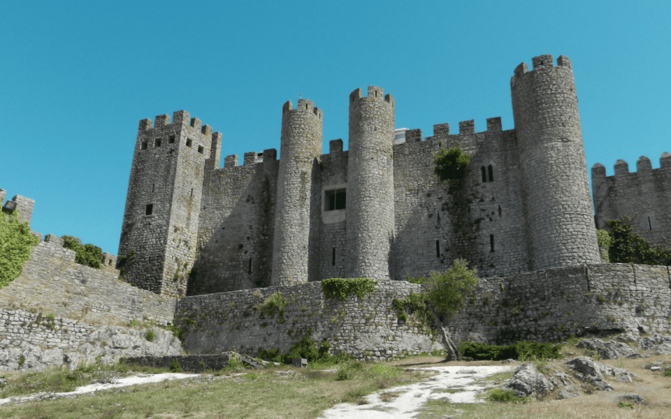 Front view of the medieval Castle of Óbidos in Portugal, featuring high stone walls, cylindrical towers, and a clear blue sky. A historic fortress and national monument showcasing Portuguese architectural heritage.