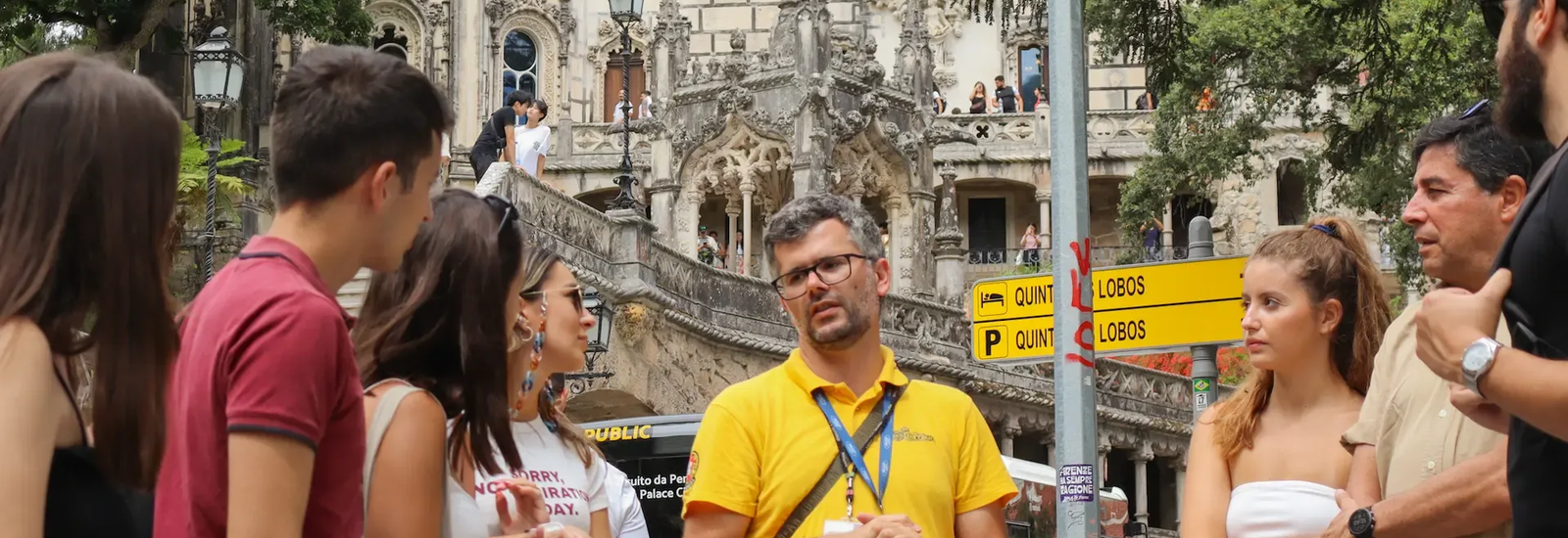 Tour guide explaining the history of the Palace of Quinta da Regaleira in Sintra, Portugal, to a group of tourists standing in front of the ornate gothic façade.