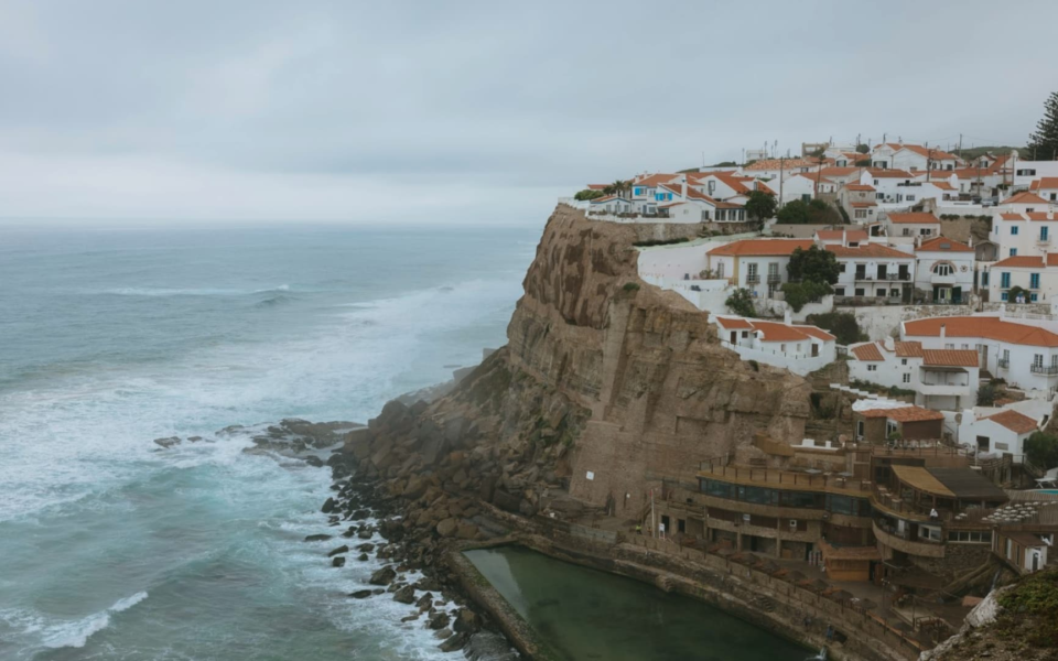 Dramatic view of Azenhas do Mar, a cliffside village in Sintra, Portugal, overlooking the Atlantic Ocean with a natural sea pool below.