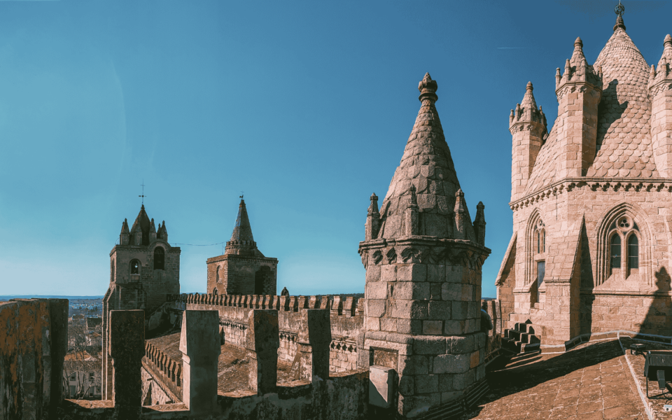 Stone towers and rooftop walkway of Évora Cathedral on a clear day in Portugal, showing Gothic architectural details and panoramic views.