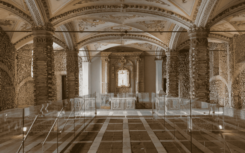 Interior of the Chapel of Bones in Évora, Portugal, featuring ornate vaulted ceilings and walls lined with human skulls and bones, creating a somber and reflective atmosphere.