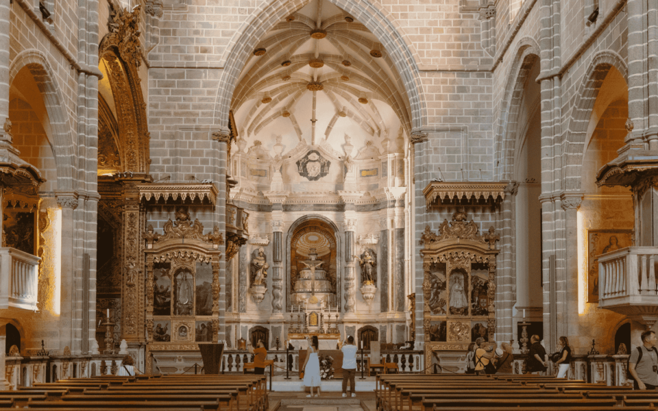 Stunning interior of Évora Cathedral in Portugal, with vaulted Gothic arches, ornate golden altarpieces, and visitors admiring the main altar.