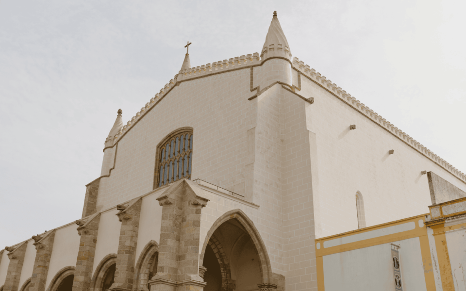 Facade of the Church of São Francisco in Évora, Portugal, with Gothic and Manueline architectural elements under a soft cloudy sky.