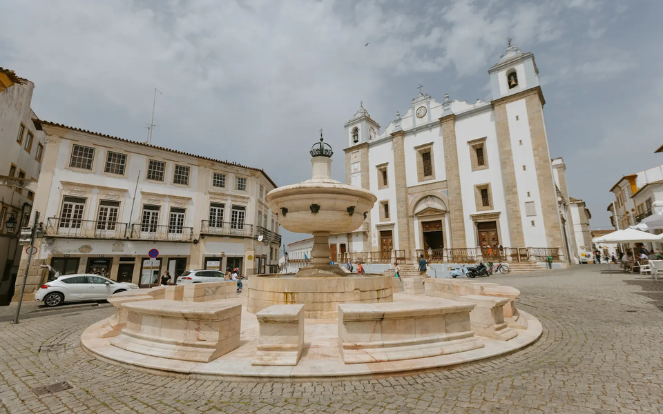 Giraldo Square in Évora, Portugal, featuring the marble Renaissance fountain and the Church of Santo Antão, surrounded by historic buildings and cobbled streets.