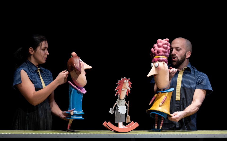 Two performers manipulate exaggerated puppets during a theatrical show