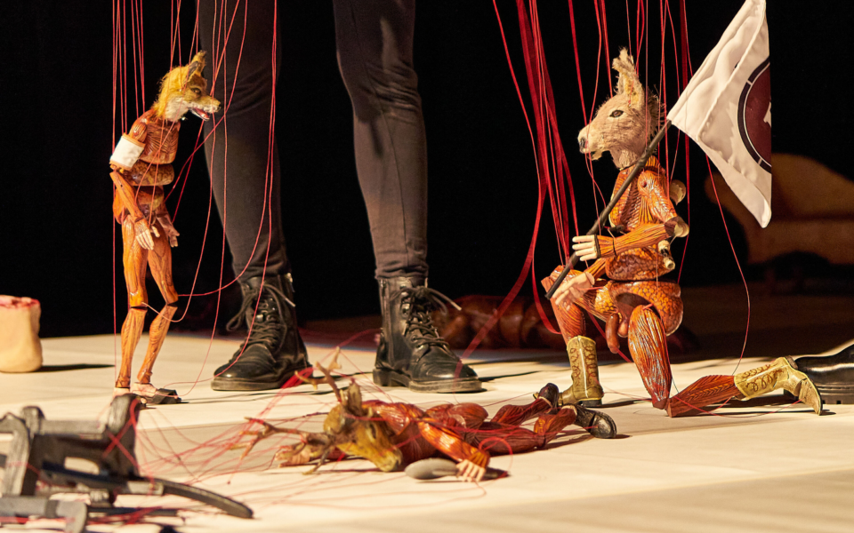 Animal-shaped puppets in a tense theatrical moment, suspended by strings