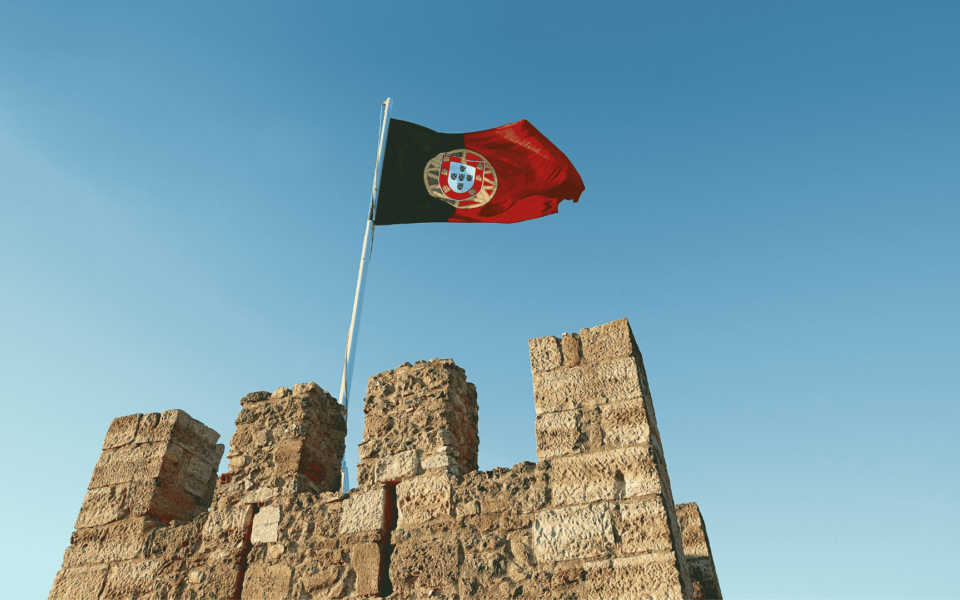 The Portuguese flag flying above the historic stone walls of Castelo de São Jorge in Lisbon, Portugal.