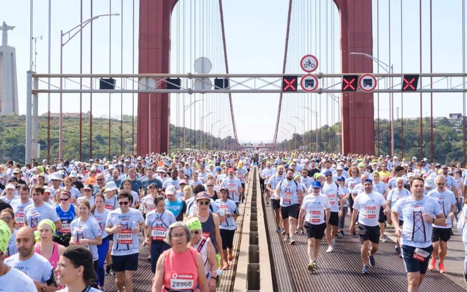 Runners crossing the 25 de Abril Bridge during the EDP Lisbon Half Marathon, with the Cristo Rei monument in the background