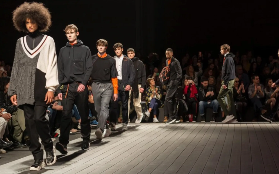 Male models walking on the runway during a menswear fashion show, wearing modern urban-inspired outfits with the audience watching