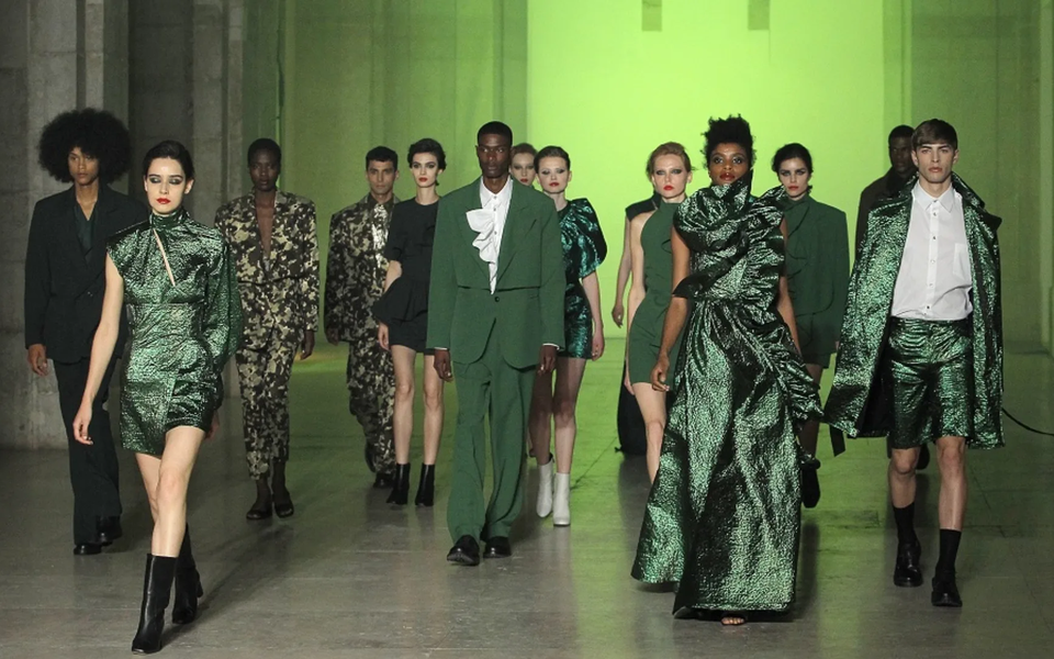 Models walking the runway at ModaLisboa fashion show, wearing green and patterned outfits with a dramatic background lighting