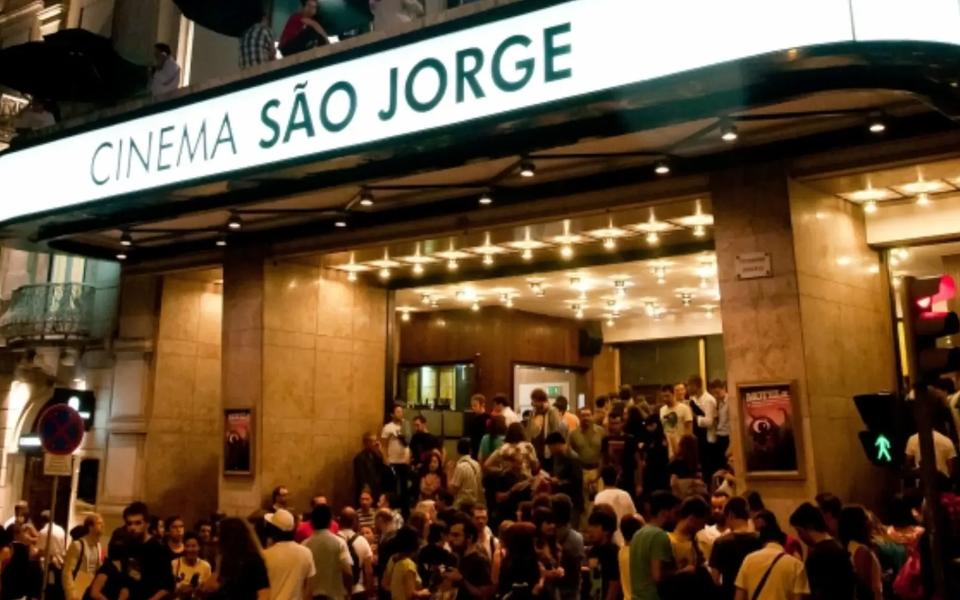 Multidão reunida à entrada do Cinema São Jorge, em Lisboa, durante a noite, com a fachada iluminada e o letreiro "Cinema São Jorge", no contexto do festival MOTELX.