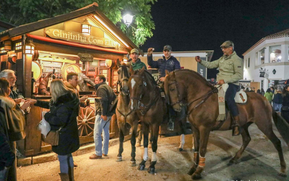 Riders on horseback toasting near a traditional ginjinha stand at the Golegã Horse Fair