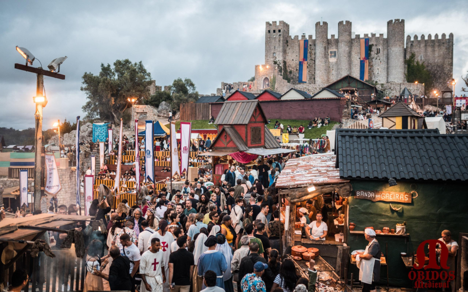 Visitors walking through medieval market stalls and taverns at Óbidos fair with the castle in the background