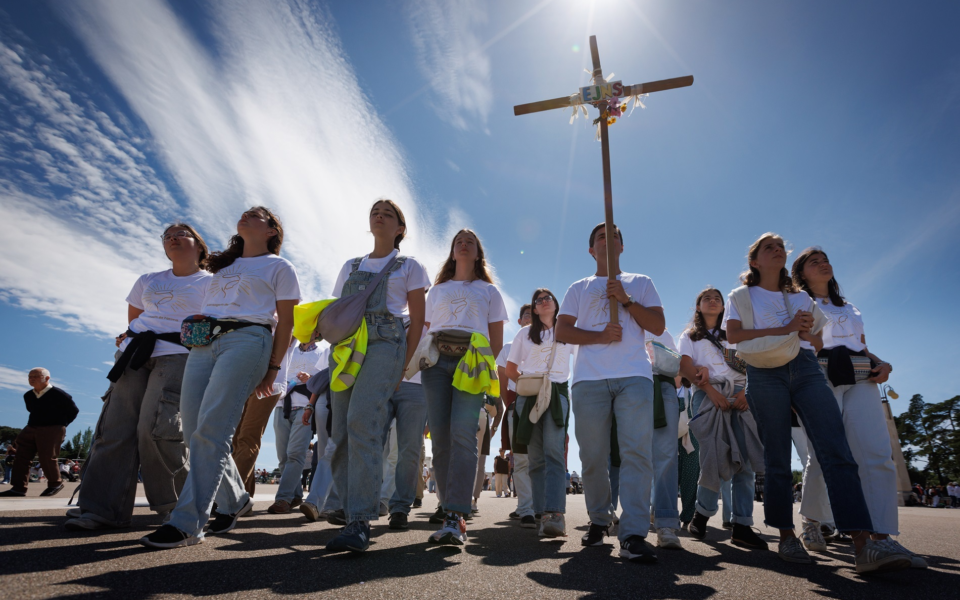 Group of young pilgrims walking towards the Sanctuary of Fátima holding a wooden cross